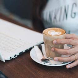 Une main tient une tasse de café posée près d'un cahier ouvert