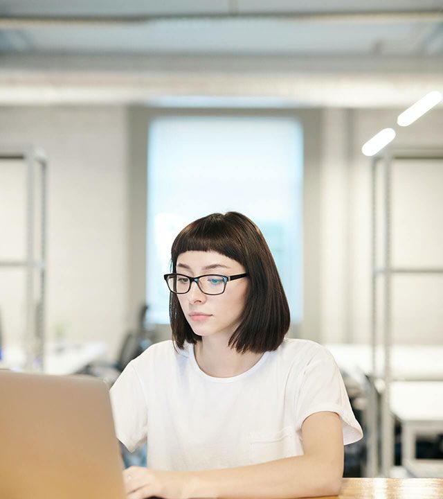Une femme à lunettes travaille sur un ordinateur portable dans un bureau clair
