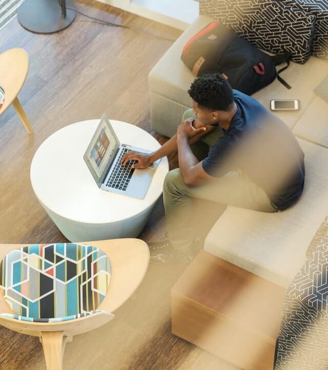 Vue de dessus : une personne assise dans un salon travaille sur un ordinateur portable posé sur une table basse